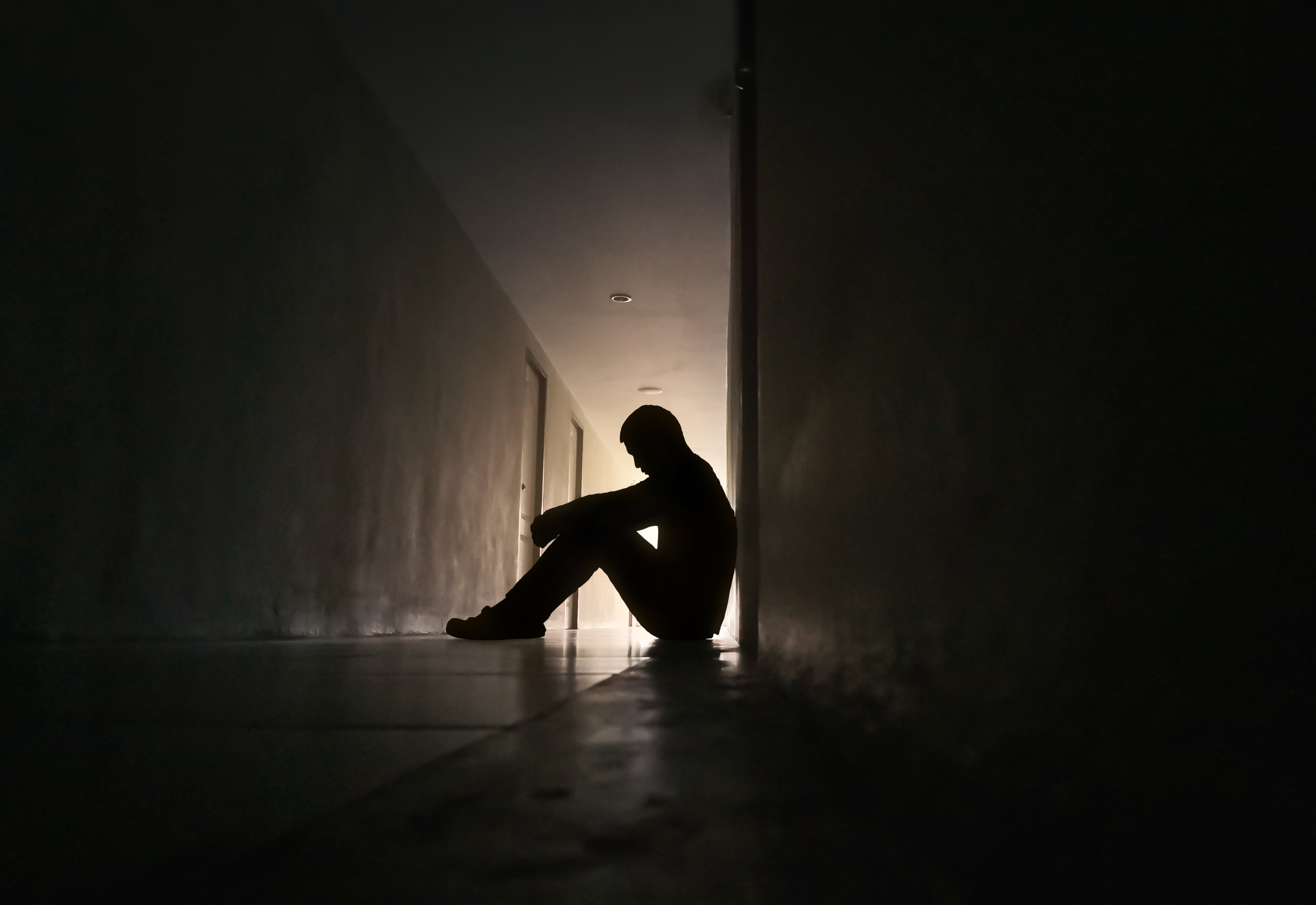 Silhouette,of,depressed,man,sitting,on,walkway,of,residence,building.